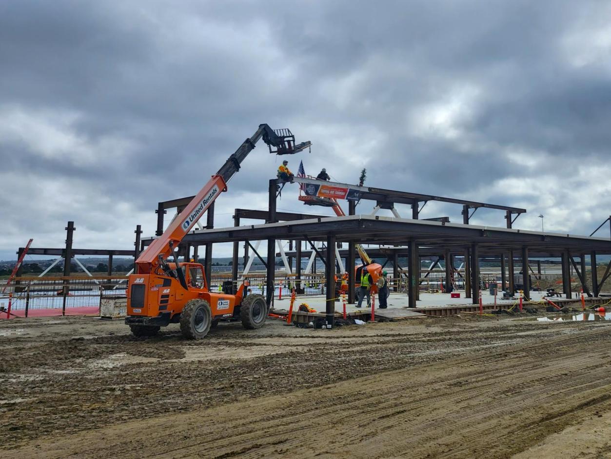 Steelworkers secure the finSteelworkers secure the final beam --"topping-out" the steel frame of the replacement passenger terminal.al beam --"topping-out" the steel frame of the replacement structure.