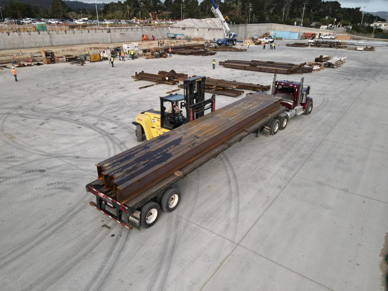 A heavy-duty forklift offloads steel girders from a flatbed trailer onto the replacement apron.