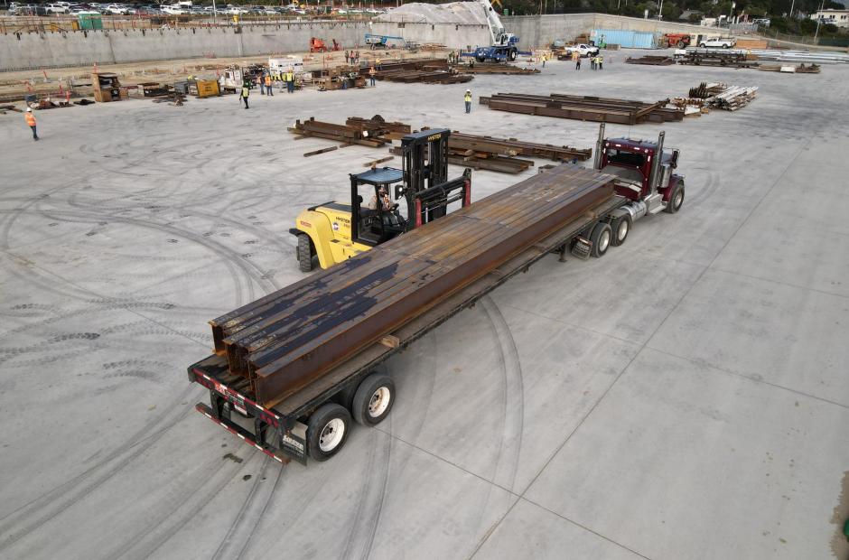 A heavy-duty forklift offloads steel girders from a flatbed trailer onto the replacement apron.