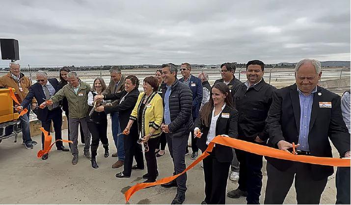 MRY Staff and Partners cut orange ribbon with Construction site and Airfield in background.